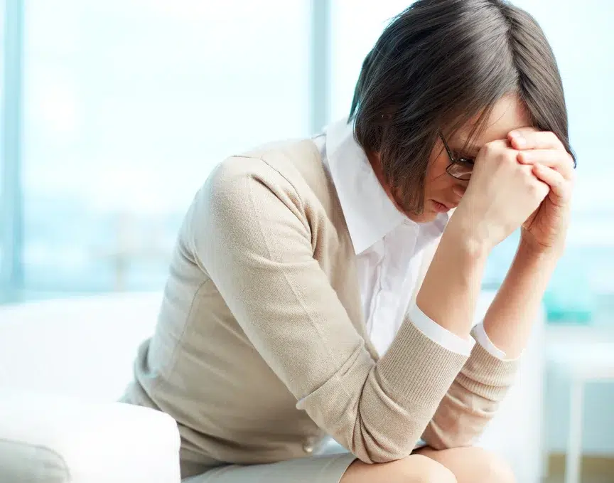 Frau mit gesenktem Kopf und gefalteten Händen zeigt Anzeichen von Stress – Symbolbild für psychosoziale Beratung bei seelischer Belastung